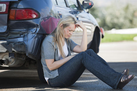 an injured woman sits on the ground by her car after a bad accident