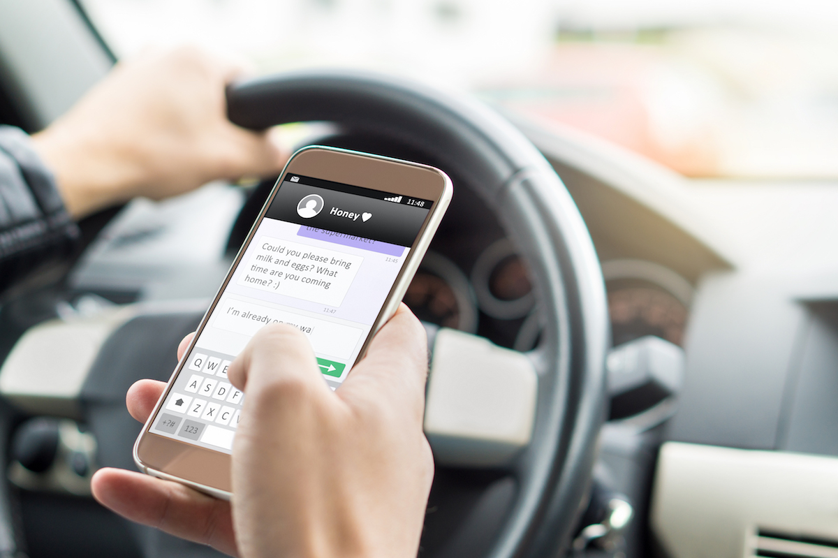 Texting while driving car. Irresponsible man sending sms and using smartphone. Writing and typing message with cellphone in vehicle.