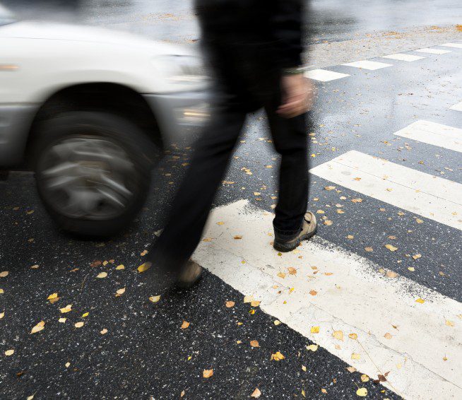 a man crossing a crosswalk is about to get hit by a car