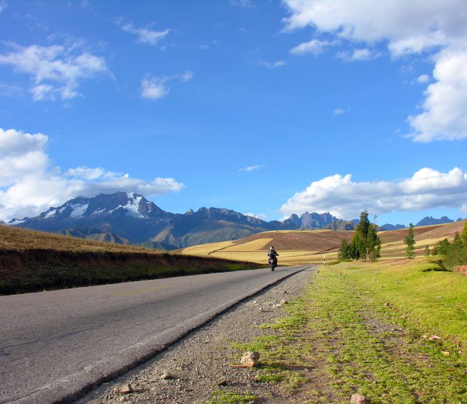 a man on a motorcycle drives on a road with mountains in the distance