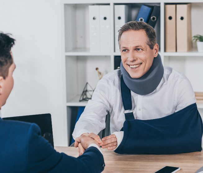 a smiling man wearing a sling shakes hands with a man in a suit