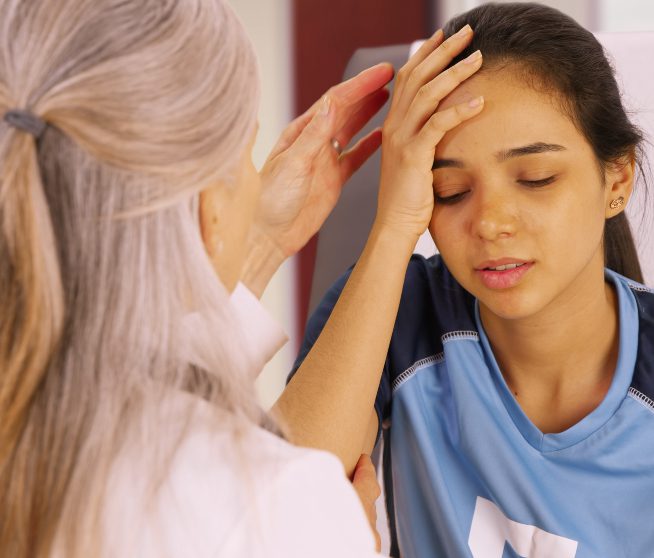 a girl in a soccer uniform holds her head in pain