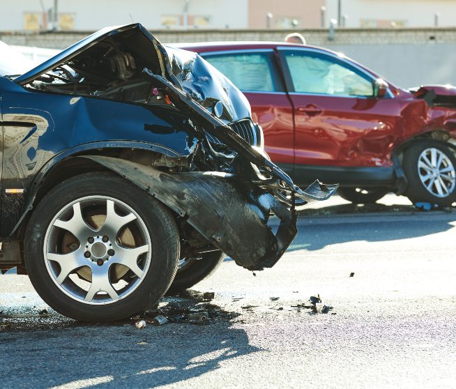 a mangled car sits in the foreground with another mangled car in the background
