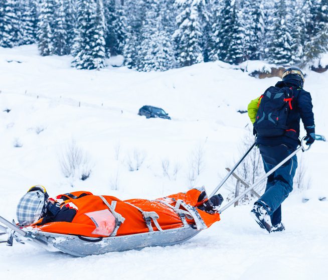 a man carries a man on a gurney down a mountain