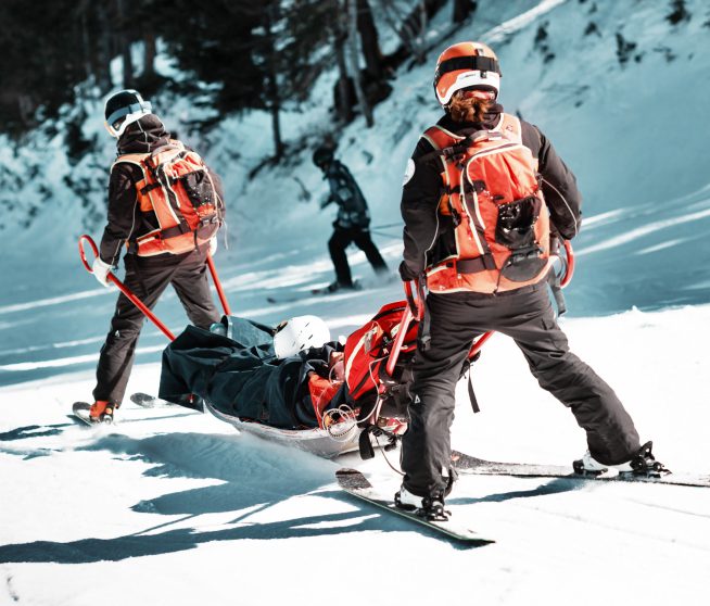 skiers carrying a man on a gurney down a mountain