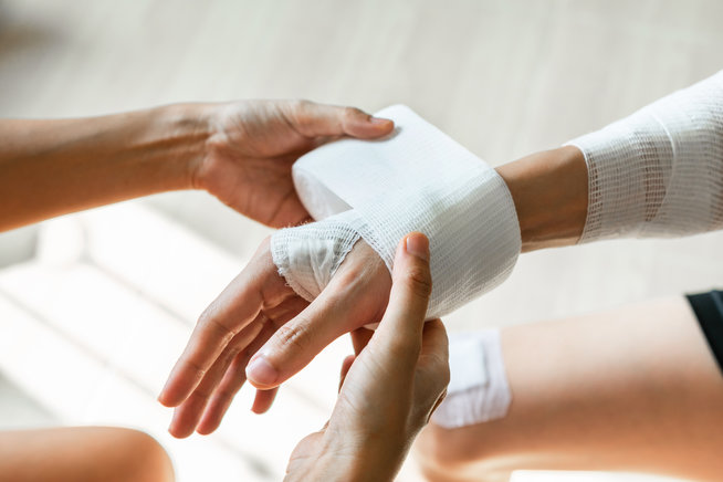Sister wrapping her brother wrist and arm with bandage around injured hand at home. First aid, accident and injury treatment concept. Closeup