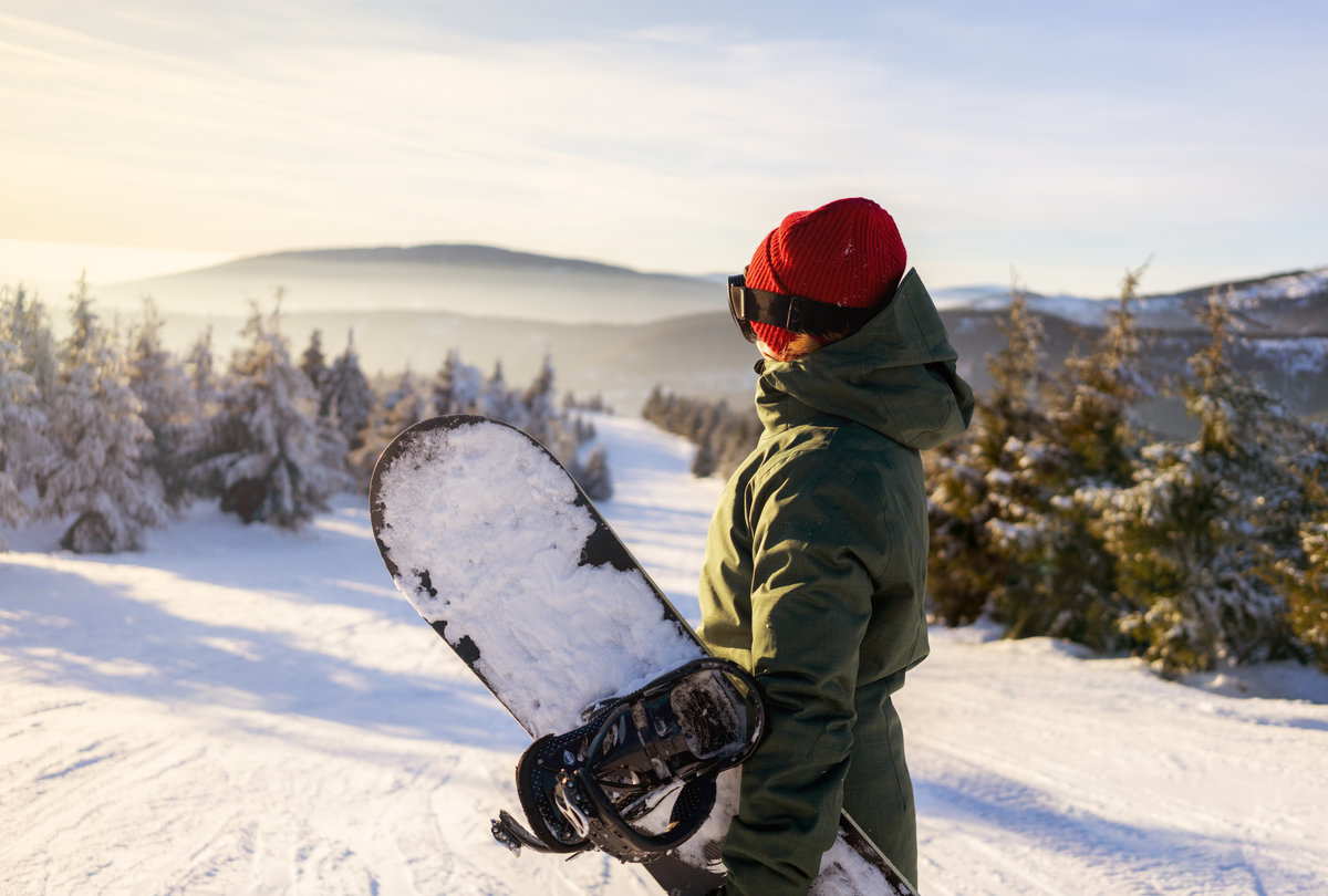 Girl snowboarder stands with snowboard on mountain's top. Ski re