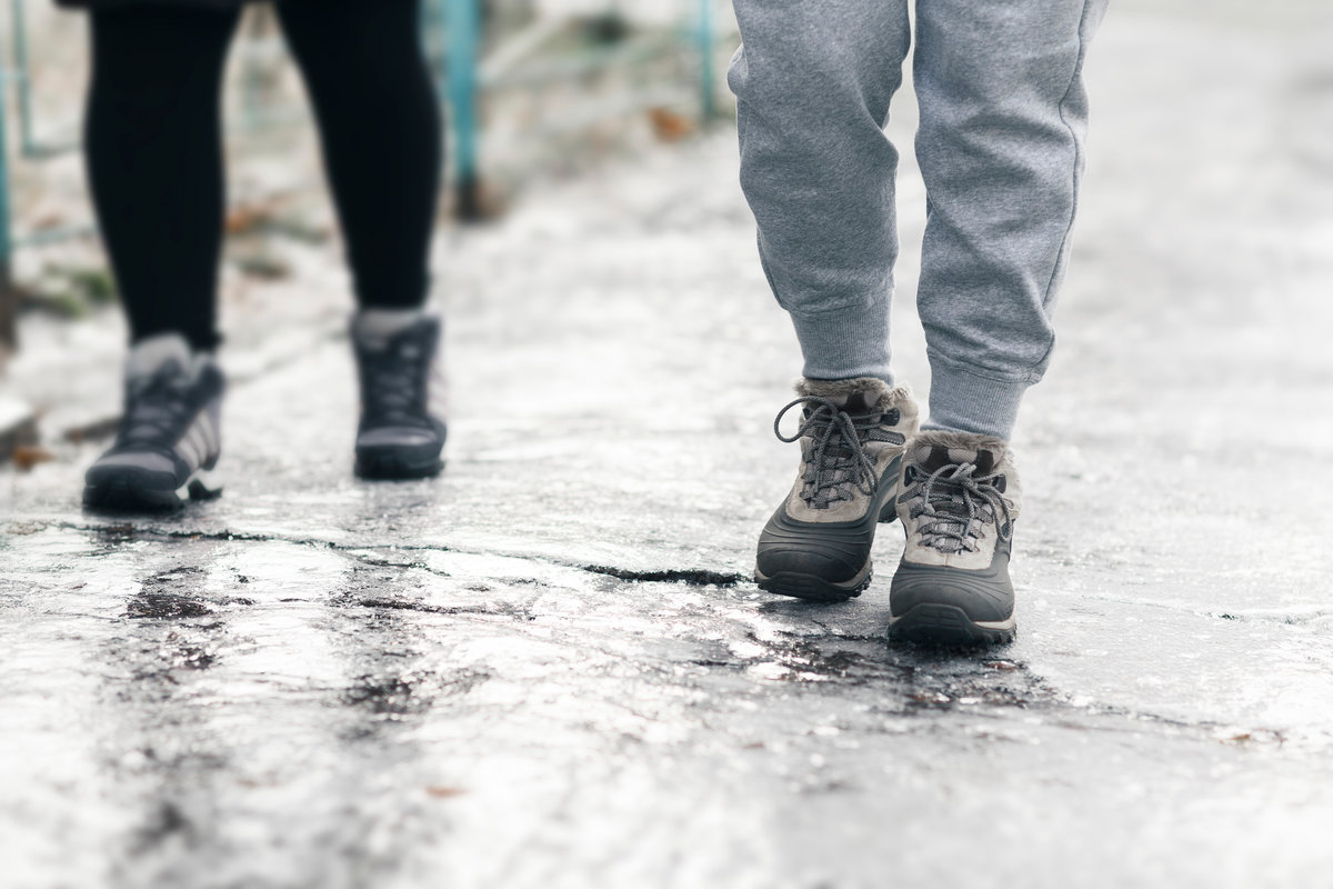 Pedestrians glide along the icy sidewalk. Winter ice on footpaths.
