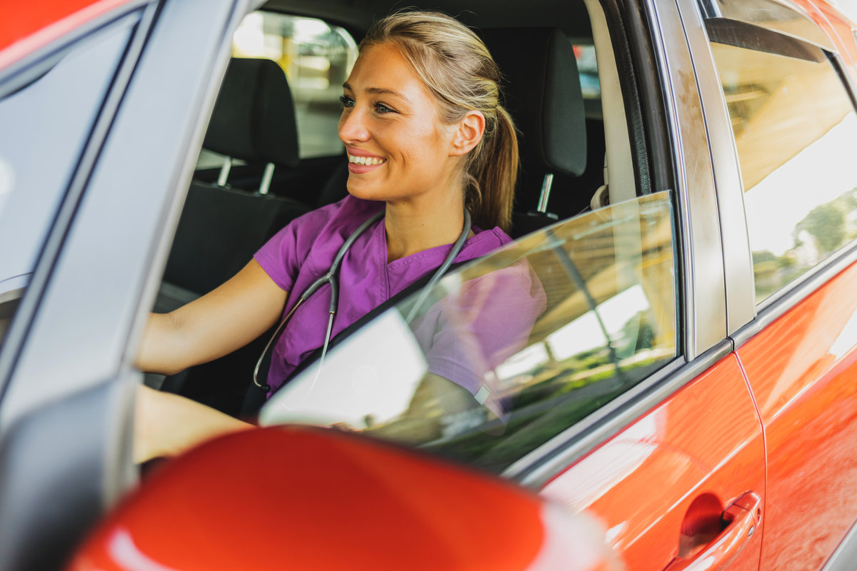 Confident medical student wearing medical scrubs while driving a car during the day. The young, female healthcare professional drives to work.
