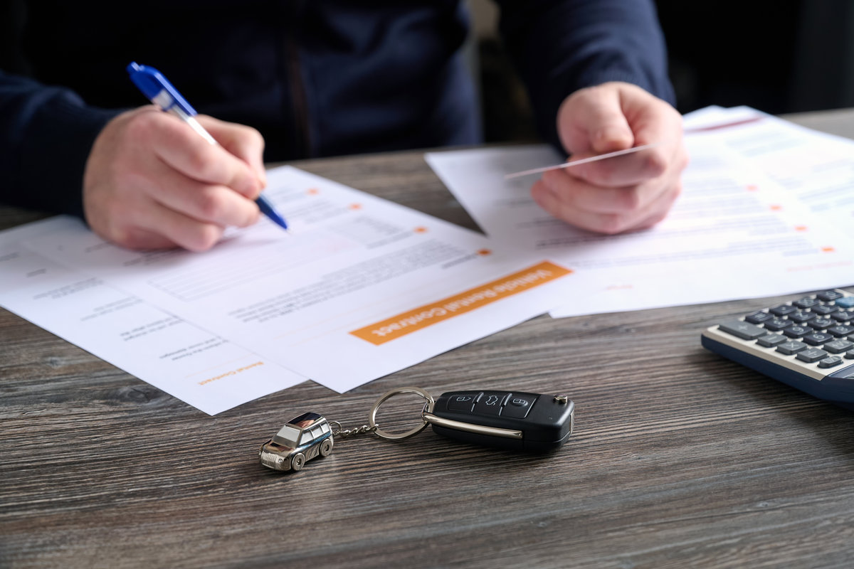 A close-up of car keys and a beautiful keychain on table. A man fills out a car rental agreement. Selective focus.